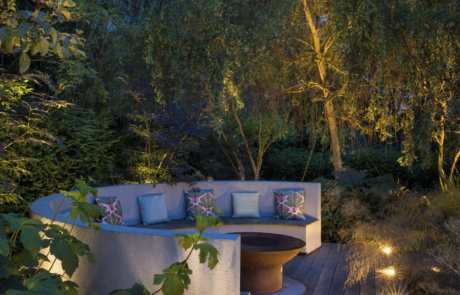 Inviting curved bench seating with corten fire pit, decking and garden lighting, in woodland garden